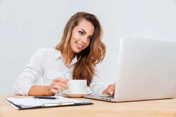 Femme d'affaires joyeuse avec tasse de café assis et utilisant un ordinateur portable — Photo