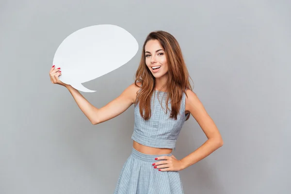 Alegre atraente jovem mulher de pé e segurando branco discurso bolha — Fotografia de Stock