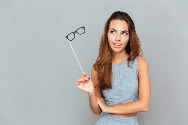Mujer joven pensativa con gafas apoyos de pie y pensando —  Fotos de Stock