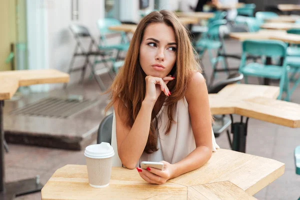 Женщина держит мобильный телефон и сидит за столом в кафе — стоковое фото