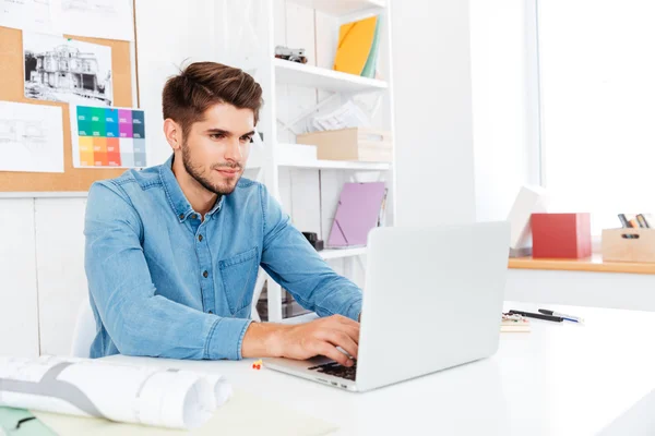 Knappe jonge casual zakenman die werken met de laptop op het kantoor — Stockfoto
