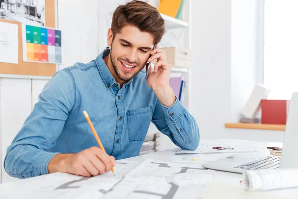 Leende ung affärsman talar på mobiltelefon och att göra anteckningar — Stockfoto