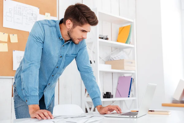 Fundersam ung affärsman använder laptop medan stående i office — Stockfoto