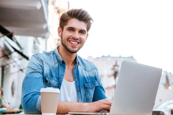 Χαμογελαστός απλός άνθρωπος χρησιμοποιώντας φορητό υπολογιστή ενώ κάθονται στο καφέ σε εξωτερικούς χώρους — Φωτογραφία Αρχείου