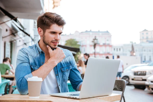 Pensativo joven hombre casual mirando portátil en la cafetería al aire libre —  Fotos de Stock