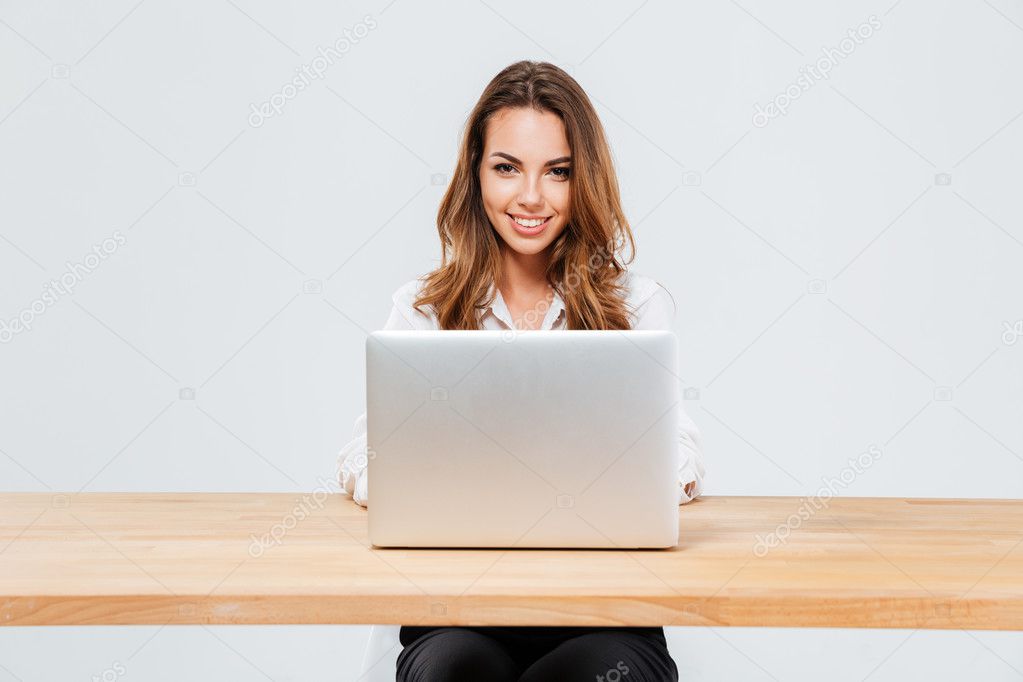 Attractive smiling businesswoman using laptop while sitting at the office