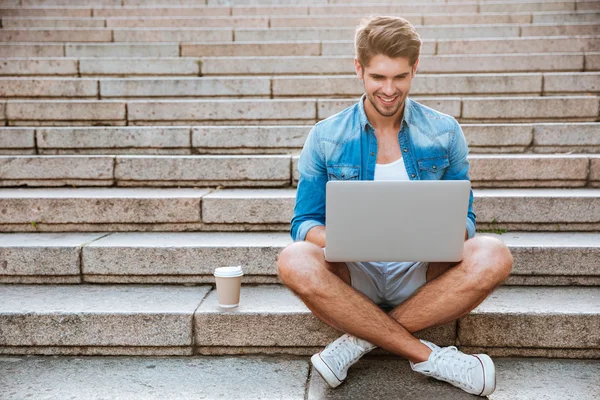 Jovem usando laptop enquanto sentado na escada ao ar livre — Fotografia de Stock