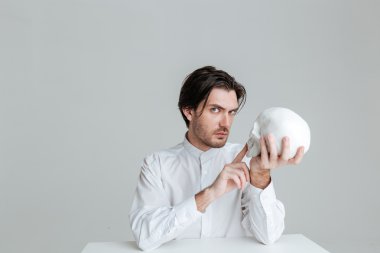 Adam oturmuş ve elinde sahte kafatası, parmak işaret