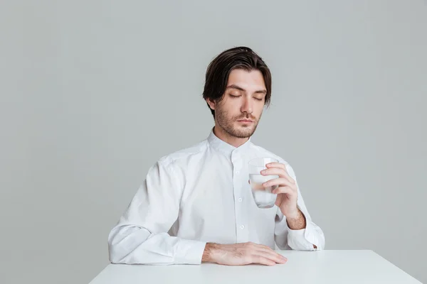 Man med ögonen stängda dricka ur vatten glas på bordet — Stockfoto