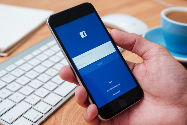 Hand holding iphone6 which displays the Facebook app