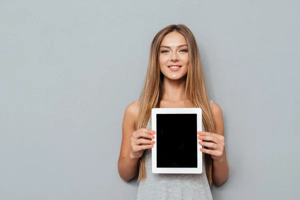 Sonriente mujer casual que muestra la pantalla de la tableta en blanco — Foto de Stock