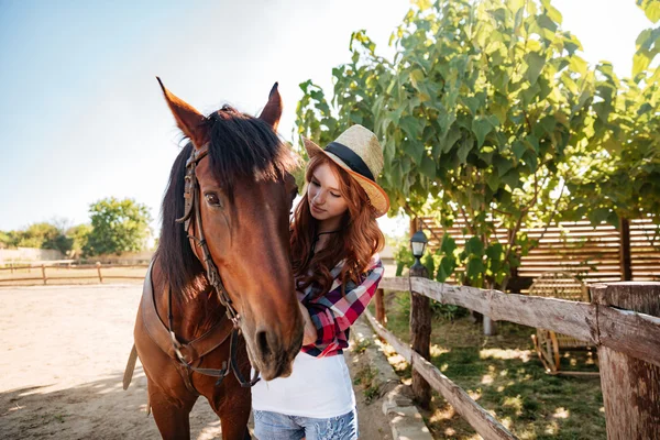 Mulher ruiva cowgirl cuidando de seu cavalo na fazenda — Fotografia de Stock