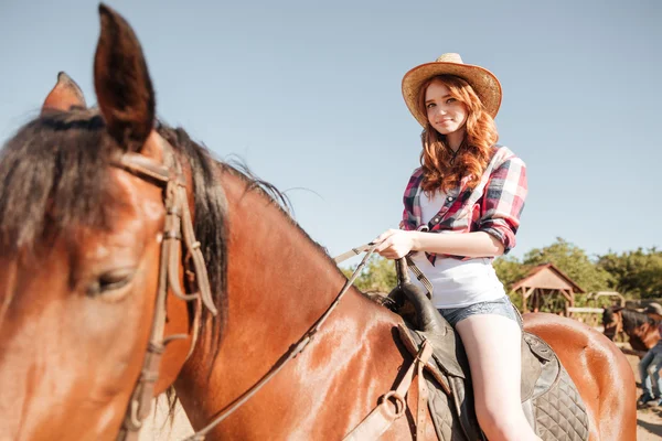 Счастливая рыжая молодая женщина ковбойша улыбается и верхом на лошади — стоковое фото