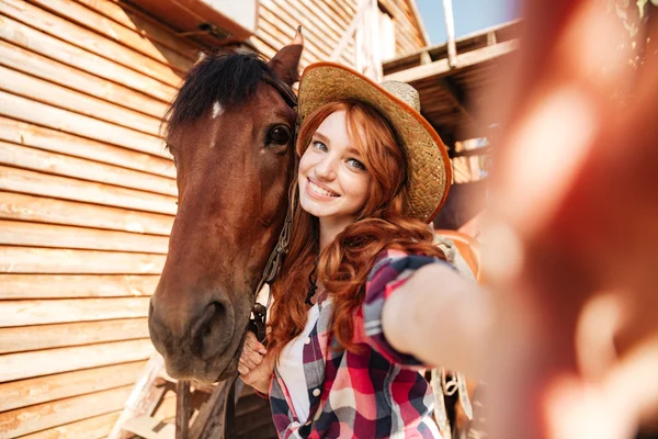 Wesoły kobieta cowgirl stojący biorąc selfie z konia w gospodarstwie — Zdjęcie stockowe