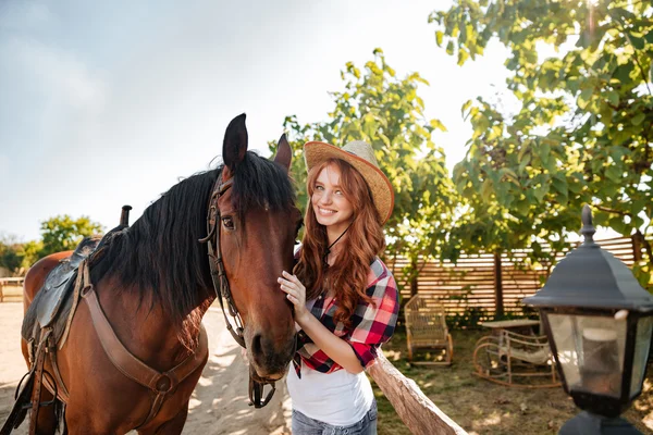 Mulher alegre cowgirl de pé com seu cavalo na aldeia — Fotografia de Stock