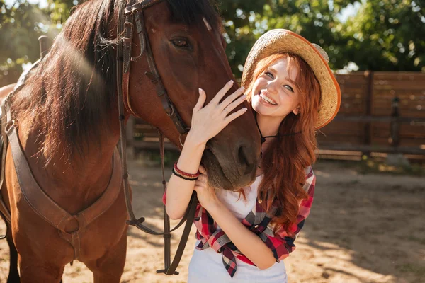 Gelukkige vrouw cowgirl in hoed permanent en knuffelen haar paard — Stockfoto