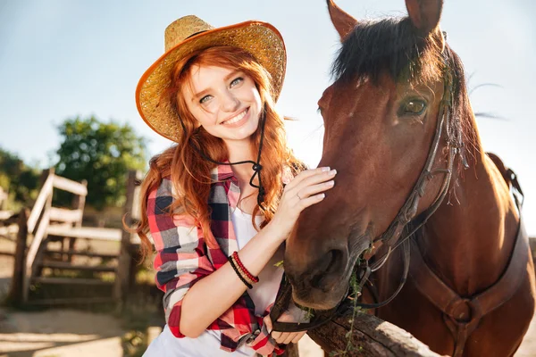 Ευτυχισμένος κοκκινομάλλα νεαρή γυναίκα καουμπόισσα στο καπέλο με το άλογό της — Φωτογραφία Αρχείου