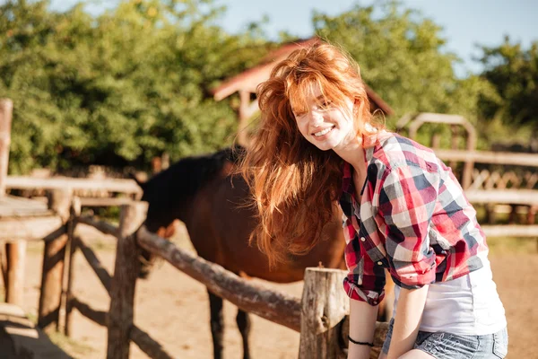 Uśmiechnięta kobieta cowgirl siedzi na ogrodzeniu w wiosce — Zdjęcie stockowe