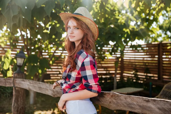 Cute Smiling Redhead Cowgirl In Hat Leaning On Ranch Fence