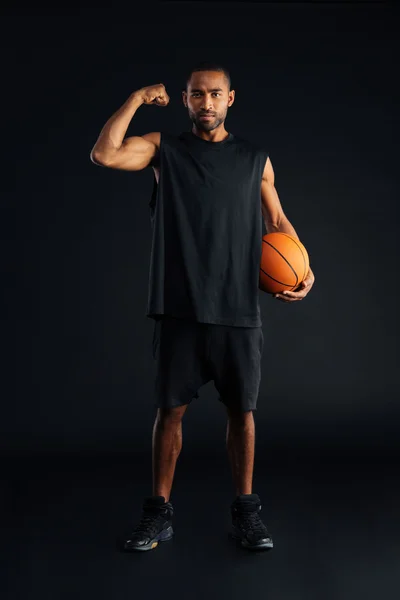 Concentrado joven jugador de baloncesto africano mostrando bíceps —  Fotos de Stock