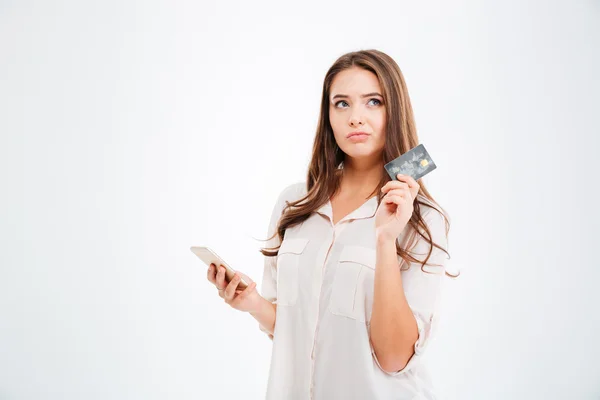 Thoughtful woman holding credit card and using smertphone Stock Picture