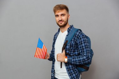 Sakallı adam sırt çantasıyla ayakta ve Abd bayrağını tutuyor