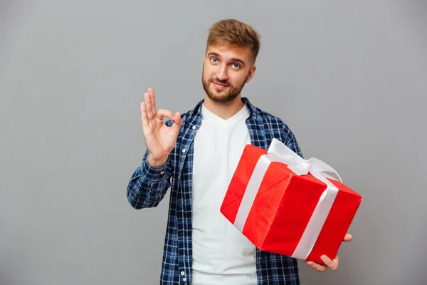 Szczęśliwy Brodaty człowiek trzyma prezent pudełko i pokazuje OK gest — Zdjęcie stockowe