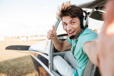 Cheerful pilot sitting in airplane cabin and showing thumbs up