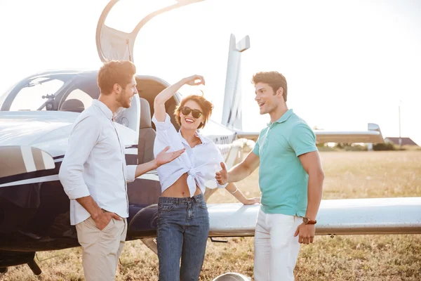 Cheerful young friends standing and talking on runway near airplane — Stock Photo, Image
