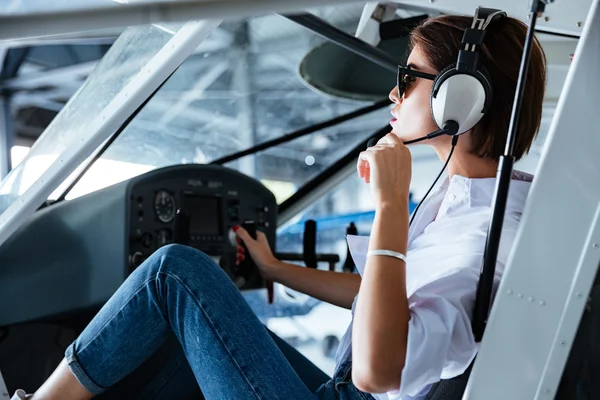 Mujer piloto sentada y hablando con auriculares en avión pequeño — Foto de Stock