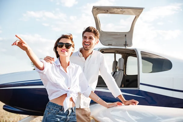 Couple standing near small plane and pointing away — Stock Photo, Image