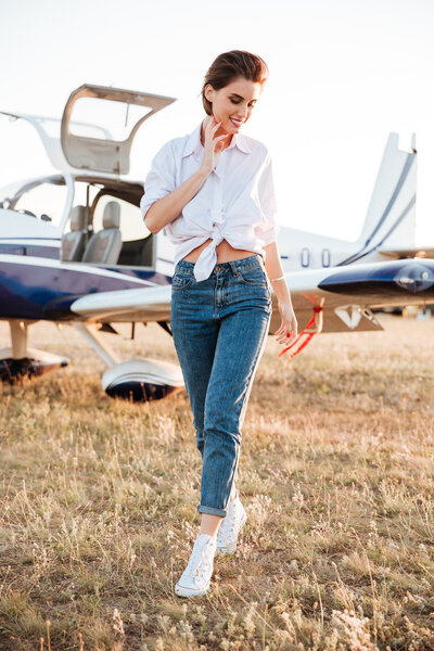 Woman walking across the field with plane on the background