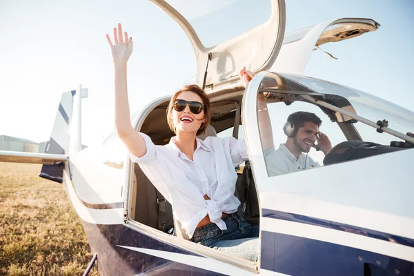 Mujer con gafas de sol saludando desde la cabina del avión después del aterrizaje —  Fotos de Stock