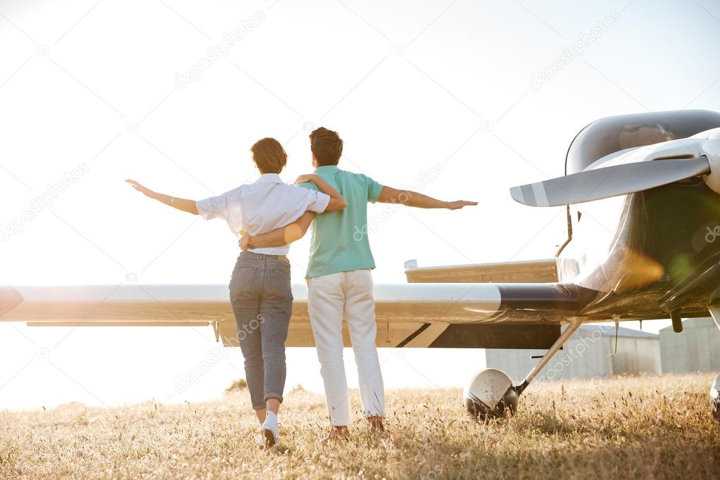 Back view of couple walking on field near small airplane