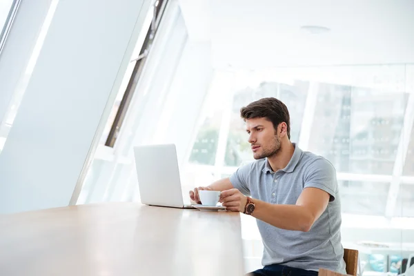 Nadenkende jongeman die werken met de laptop terwijl het hebben van koffiepauze — Stockfoto