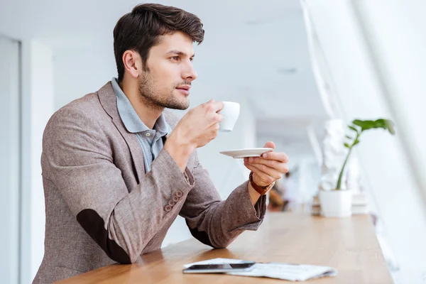 Casual young businessman drinking coffe while sitting in cafe — Stock fotografie