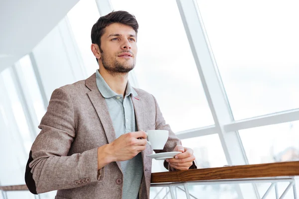 Pensativo joven hombre de negocios en chaqueta con taza de café en el interior — Foto de Stock