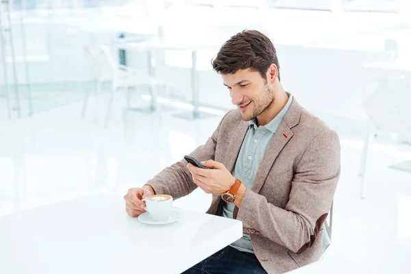 Uśmiechnięty młody biznesmen pisania wiadomości na smartfonie, siedząc — Zdjęcie stockowe