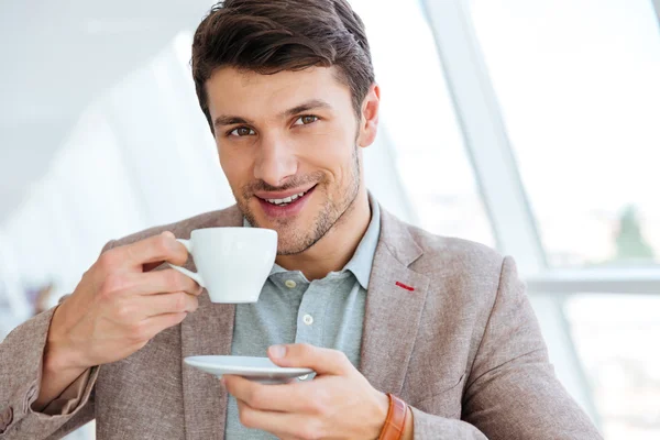 Feliz hombre de negocios sonriente con chaqueta bebiendo café en el interior — Foto de Stock