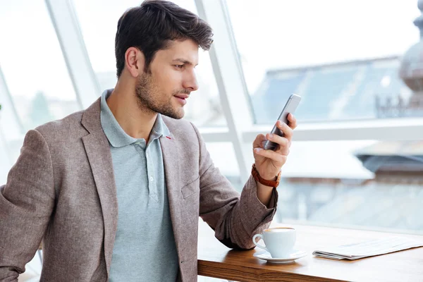 Man in jacket texting message on smartphone while sitting indoors — Stock fotografie