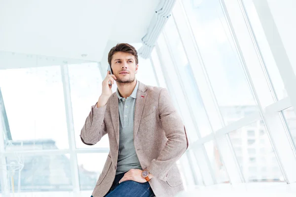 Attractive young businessman talking on mobile phone while sitting — Stockfoto