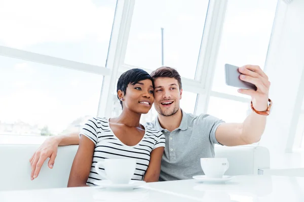 Smiling young couple making selfie photo on smartphone indoors — Stock Photo, Image