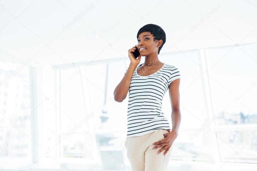 Cheerful young businesswoman standing and talking on mobile phone