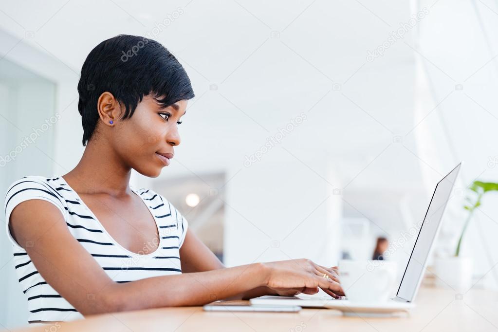 Attractive african businesswoman working with laptop and drinking coffee