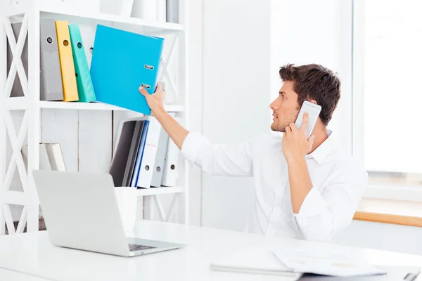 Jovem empresário levando pasta de prateleira e falando no telefone — Fotografia de Stock