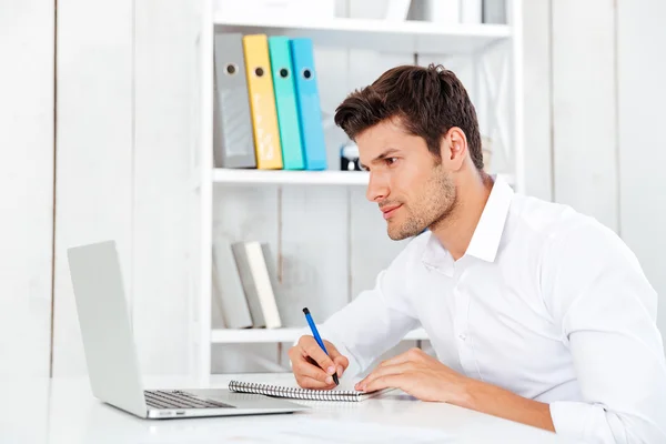 Closeup of smiling young businessman sitting and writing in notepad — ストック写真