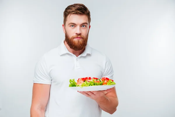 Retrato de um homem barbudo que esconde a placa com salada fresca — Fotografia de Stock