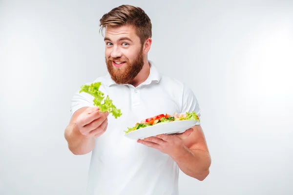 Улыбающийся мужчина держит зеленый салат и тарелку со свежим салатом — стоковое фото