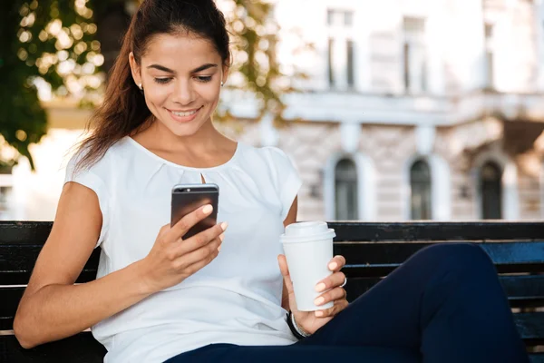 Menina bonito feliz usando telefone celular enquanto sentado ao ar livre — Fotografia de Stock