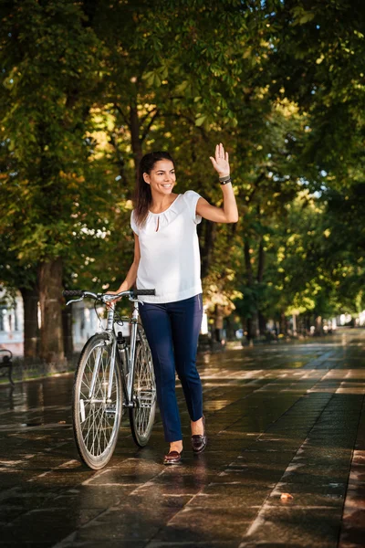Счастливая улыбающаяся девушка машет рукой с велосипедом — стоковое фото